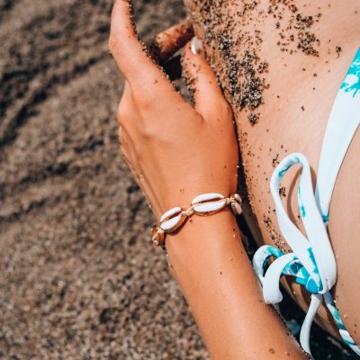 Woman's hands with shell jewelry in sand. Sand in hands on the beach. Travel and vacation concept. Female slim legs. Summertime relax